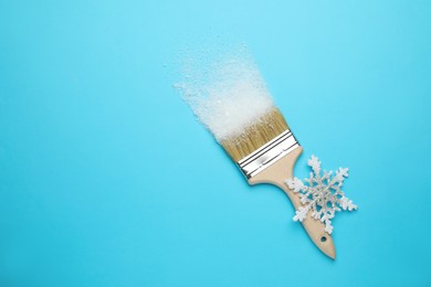 Photo of Brush painting with artificial snow on light blue background, top view. Space for text. Creative concept