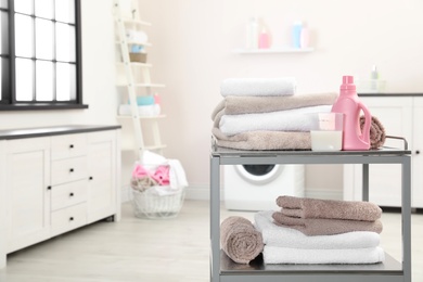 Soft bath towels and detergent on metal cart against blurred background, space for text
