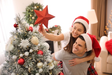 Photo of Couple decorating Christmas tree indoors, focus on star topper
