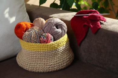 Photo of Soft woolen yarns, knitting and needles on brown sofa indoors