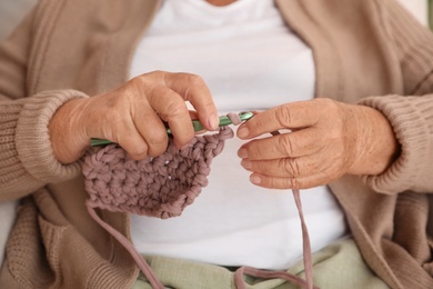 Elderly woman crocheting at home, closeup. Creative hobby