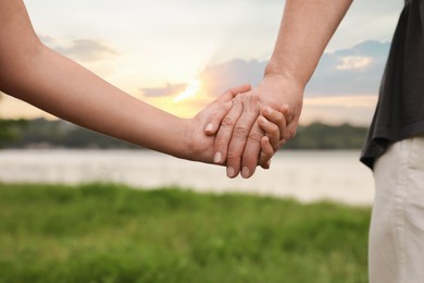 Photo of Little girl and grandmother holding hands together in park, closeup