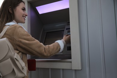 Photo of Young woman using cash machine for money withdrawal outdoors