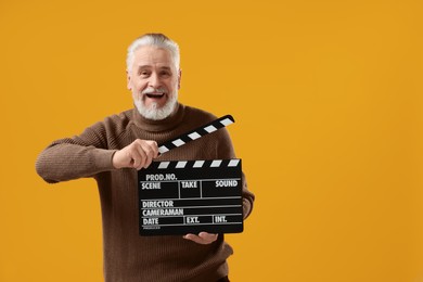 Photo of Senior actor holding clapperboard on yellow background, space for text. Film industry