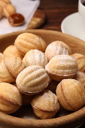 Photo of Delicious nut shaped cookies with boiled condensed milk and powdered sugar in wooden table, closeup