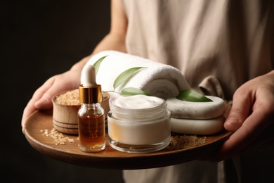 Woman holding products for spa procedures on dark background, closeup