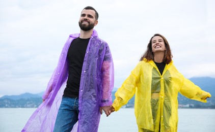 Young couple in raincoats enjoying time together under rain on beach