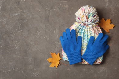 Stylish blue woolen gloves, hat and dry leaves on grey table, flat lay. Space for text