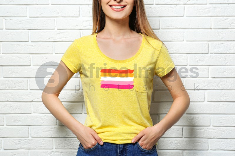 Young woman wearing yellow t-shirt with lesbian flag near white brick wall. LGBT concept