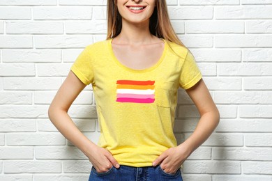 Young woman wearing yellow t-shirt with lesbian flag near white brick wall. LGBT concept