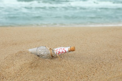 Glass bottle with SOS message on sand near sea