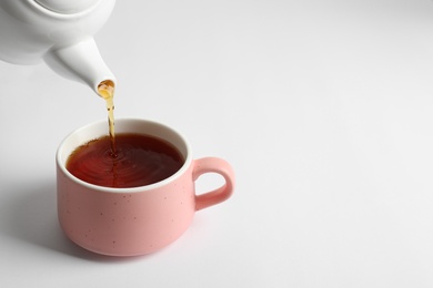 Pouring hot tea into ceramic cup on white background