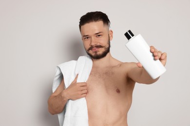 Naked man with towel and bottle of shampoo on light grey background