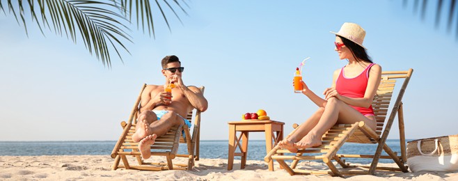 Couple with drinks resting on sunny beach at resort. Banner design