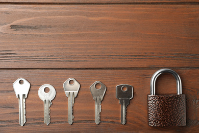Steel padlock and keys on wooden background, flat lay with space for text. Safety concept