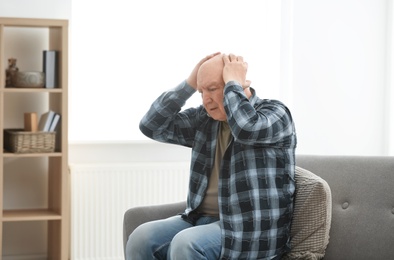 Depressed senior man sitting on sofa indoors
