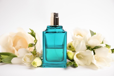 Bottle of perfume and beautiful flowers on white background