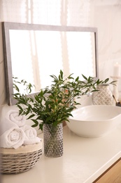 Vase with beautiful branches and fresh towels near vessel sink in bathroom. Interior design