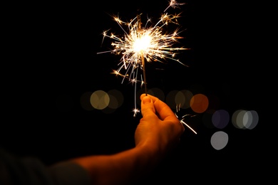 Woman holding bright burning sparklers against blurred lights, closeup