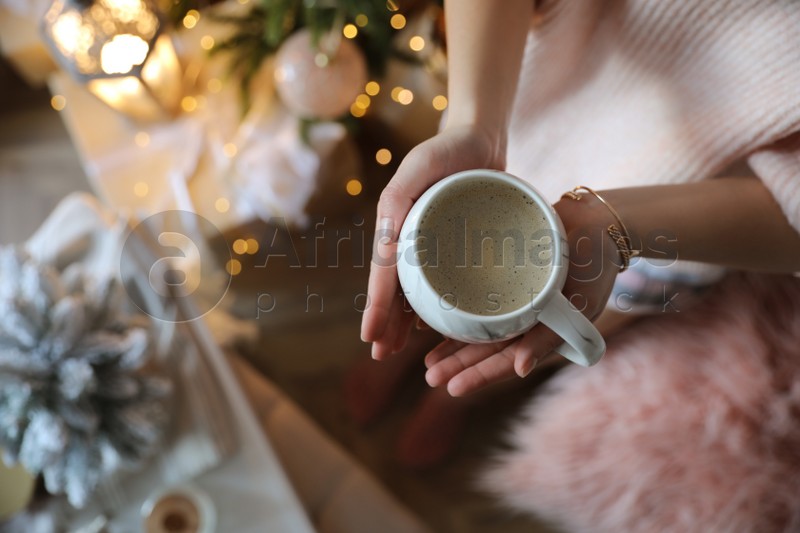 Woman with cup of cocoa in room decorated for Christmas, top view