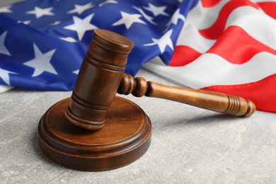 Judge's gavel and American flag on light grey table, closeup