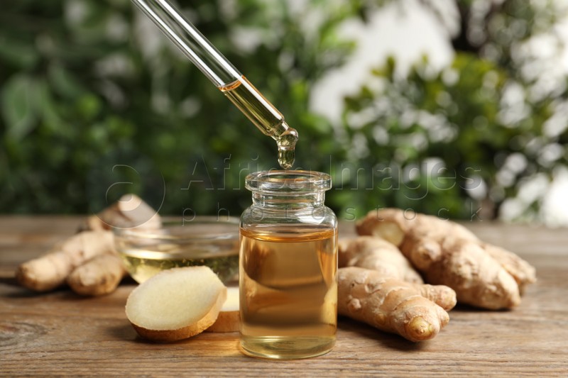 Photo of Dripping ginger essential oil from pipette into bottle on wooden table
