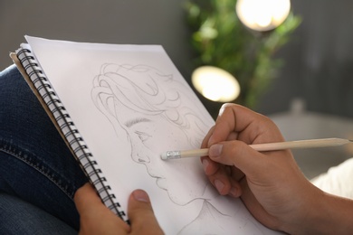 Photo of Man drawing portrait with pencil in notepad indoors, closeup