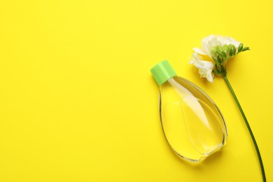 Bottle of baby oil and blooming freesia on yellow background, flat lay. Space for text