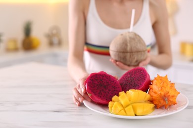 Photo of Young woman with fresh exotic fruits at table in kitchen, closeup. Space for text