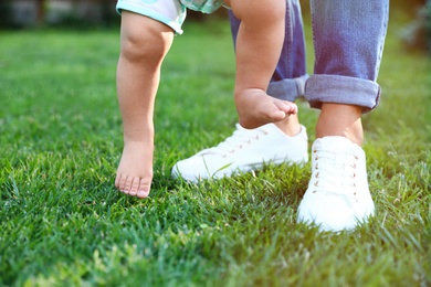 Cute little baby learning to walk with his nanny on green grass outdoors, closeup