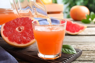 Pouring delicious grapefruit juice into glass on wooden table