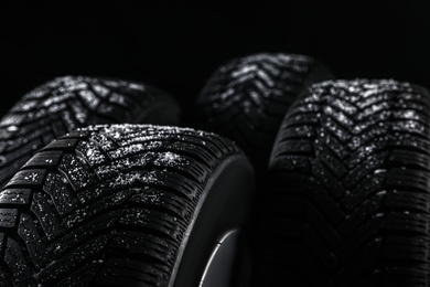 Snowy set of wheels with winter tires on black background, closeup. Space for text