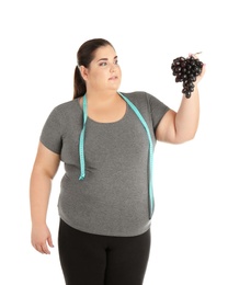 Overweight woman with grapes and measuring tape on white background