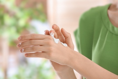 Young woman applying cream on her hands indoors, closeup