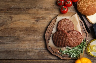 Tasty grilled hamburger patties, vegetables, rosemary and bun on wooden table, flat lay. Space for text