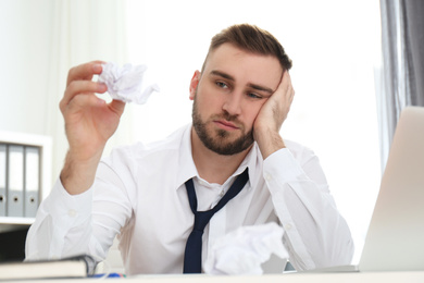 Lazy young man with crumpled paper at messy table in office