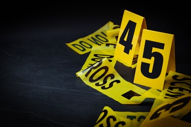 Crime scene tape and evidence markers on black slate background, closeup. Space for text