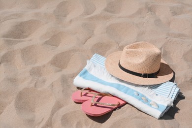 Straw hat, beach towel, seashells and flip flops on sand, space for text