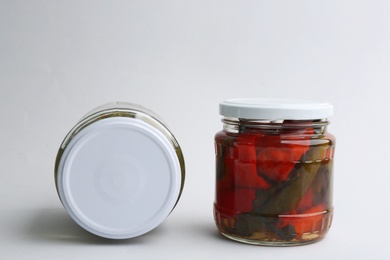 Glass jars with pickled bell peppers and cucumbers on white background