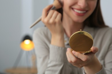 Photo of Young woman with cosmetic pocket mirror doing makeup indoors, closeup