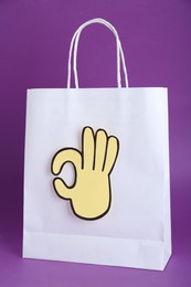 Photo of Paper bag and cutout of okay hand gesture on purple background