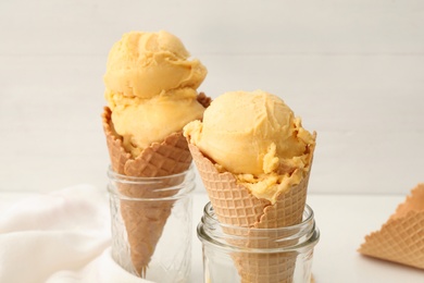 Delicious yellow ice cream in wafer cones and glass jars on table, closeup
