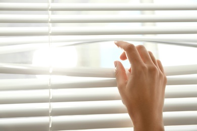 Woman opening horizontal window blinds at home, closeup. Space for text