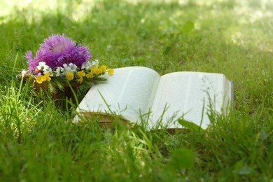 Open book and beautiful wildflowers on green grass outdoors