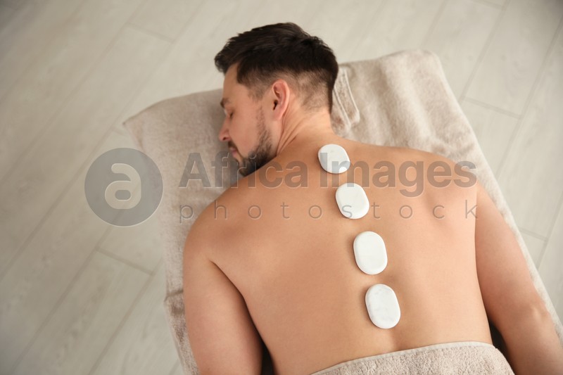 Photo of Handsome man receiving hot stone massage in spa salon, above view. Space for text