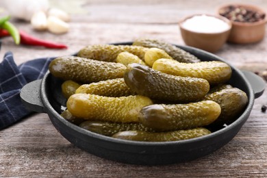 Pickled cucumbers in pan on wooden table, closeup