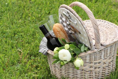 Photo of Picnic basket with wine, bread and flowers on green grass outdoors