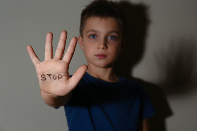 Photo of Abused little boy showing palm with word STOP near beige wall, focus on hand. Domestic violence concept