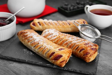 Photo of Fresh tasty puff pastry with sugar powder served on grey table, closeup