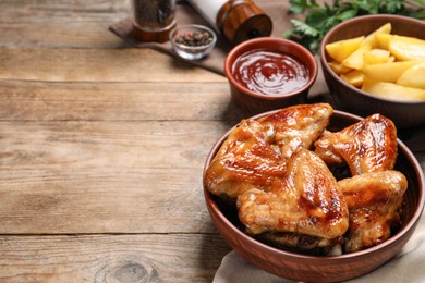 Bowl with delicious fried chicken wings on wooden table, space for text